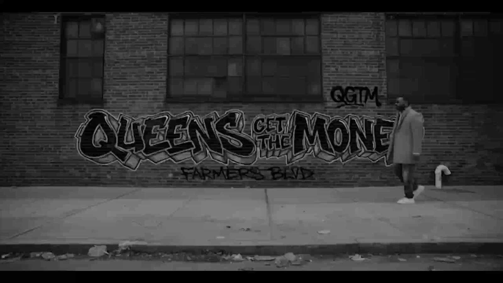 A man walking past a Queens Get The Money mural on Farmers Boulevard